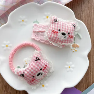 Close-up of pink plaid bear hair tie and lace trim clip in a decorative ceramic dish