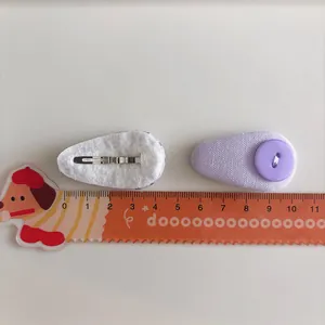 Detail showing two purple fabric drop hair clips with button decor and metal snap back