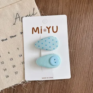 Close-up of blue fabric teardrop hair clips with polka dots and button on a display card
