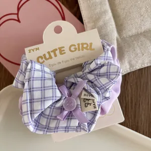 Detailed shot of lilac plaid scrunchie with ribbon bow and button on packaging card