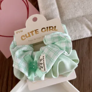Detail of light green plaid fabric scrunchie with handmade label and button decor