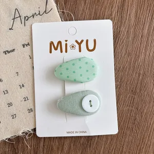 Detailed shot of two green fabric hair clips with dots and buttons on a paper card