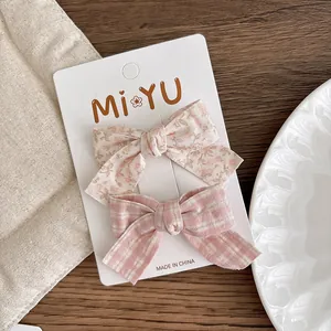 Detailed pair of floral and plaid fabric bow hair clips displayed on a white branded card