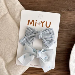 Close-up of blue plaid and bow pattern fabric hair clips on a branded display card