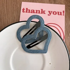 Détail de deux pinces à cheveux en forme de cœur en denim bleu foncé sur un plateau