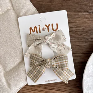Set of two fabric bow hair clips with floral and plaid patterns on display card