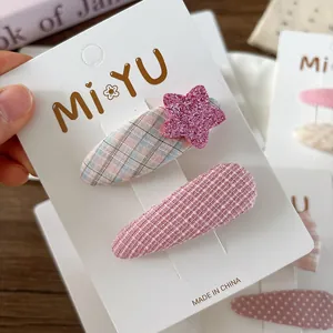 Detail of pink plaid hair clips with glitter star on a white display card over wood
