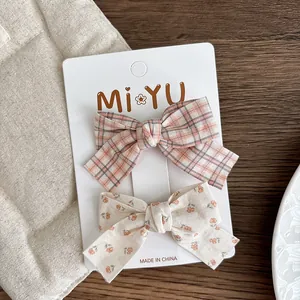Detail of two fabric bow hair clips with floral and plaid patterns on display card