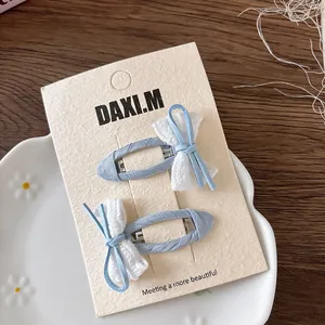 Close-up of blue plaid bow hair clips with white lace on a minimalist display card
