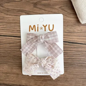 Detail of plaid and floral fabric bow hair clips on a white card tag with a wood background