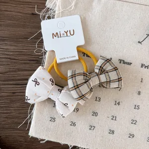 Detail view of plaid and floral fabric bow hair ties on cream elastic bands