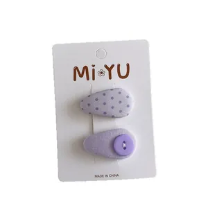 Set of two purple fabric waterdrop hair clips with polka dots and button on a white card
