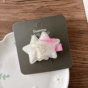 Vue macro d'une barrette étoile avec paillettes crème et nœud rose sur support carton