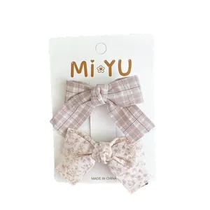 Set of two fabric bow hair clips featuring pink plaid and lilac floral patterns on card