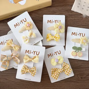 Set mit gelben Stoff-Schleifen und Blumen-Haarspangen für Mädchen auf einem Holztisch