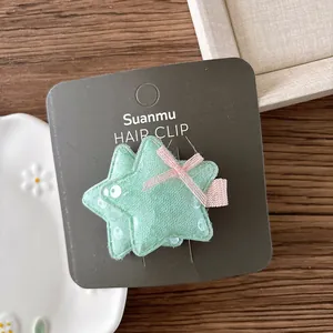 Détail de barrettes étoiles vertes pailletées avec nœuds roses sur carte de marque