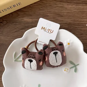 Detail of two plush brown bear hair ties with embroidery on a ceramic flower plate