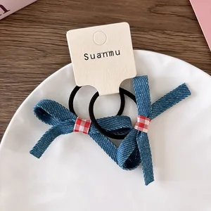 Close-up of denim bow hair ties with red gingham detail on a white ceramic plate