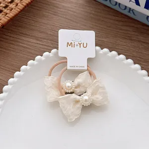Dettaglio di elastici per capelli con fiocco beige e perle eleganti su cartoncino