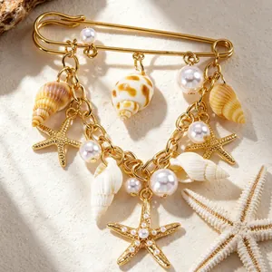 Détail d'une broche de style plage dorée avec des étoiles de mer coquillages et perles
