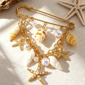Vue détaillée des breloques étoile de mer et perles sur une broche épingle de nourrice dorée.