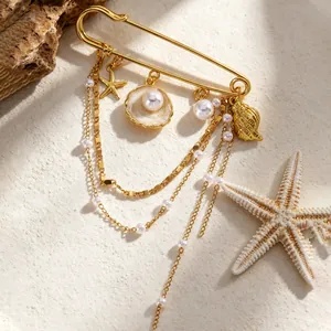 Détail d'une broche dorée avec pendentifs étoile de mer coquillage et perles sur sable.