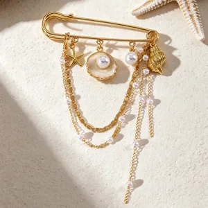 Broche océan dorée avec pendentifs étoile de mer coquillage et perles sur sable.