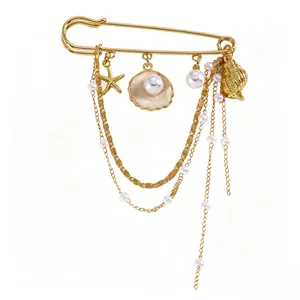Gros plan d'une broche en épingle dorée avec breloques étoile de mer, coquillage et perles.