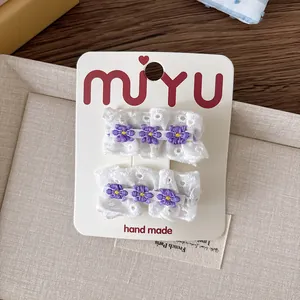 Détail de barrettes en dentelle faites main avec broderies de fleurs violettes