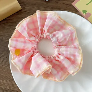 Primer plano de un coletero de tela vichy rosa con un pequeño dije amarillo en un plato