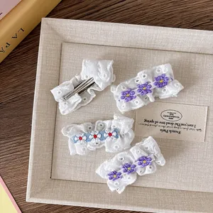 Détail de fleurs brodées sur barrettes en dentelle blanche avec pinces en métal