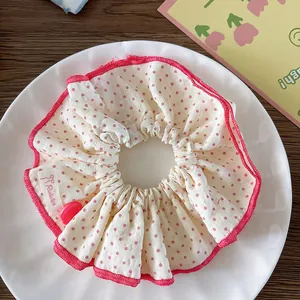 Detalle de un coletero de tela blanca con lunares rosas, un botón y una etiqueta tejida