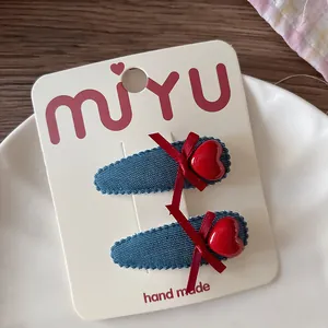 Détail de deux barrettes en denim avec cœurs rouges et nœuds sur carton blanc