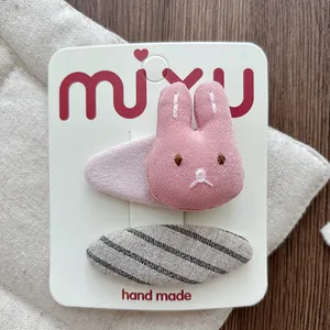 Detailed close-up of pink plush bunny hair clip and grey striped fabric barrette on card