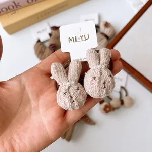 Close-up of cute beige plush rabbit hair tie with pearl detail and soft knitted texture