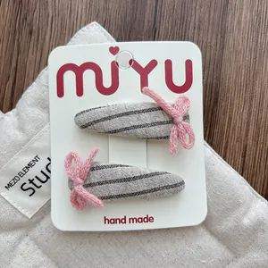 Detail of pink knitted bow hair clips with grey striped fabric on white display card