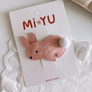 Detail of pink cartoon rabbit hair clip with white pompom on branded display card