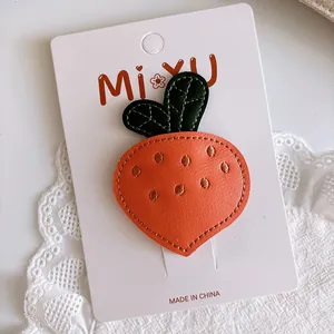 Detailed view of a handmade leather carrot hair clip with green leaves on a display card