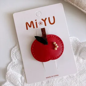 Detail of a red leather apple hair clip with green leaf on a white display card