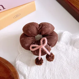 Detail of a brown fabric scrunchie with a pink knit bow and fuzzy plush ball accents
