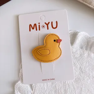 Detail of yellow leather cartoon duck hair clip showing fine stitching on white lace