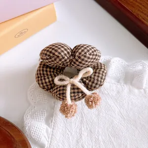 Close-up of a brown plaid hair scrunchie with a cream bow and soft pompom charms