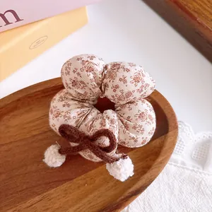 Detailed shot of plaid scrunchie with brown woven bow and soft white plush pompoms