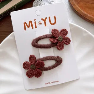 Detail of two handmade knit flower hair clips in dark red and green on a white card