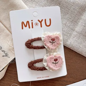 Détail de pinces à cheveux cœur brodées avec peluche rose et bordure en dentelle