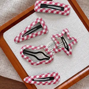 Détail de barrettes à carreaux rouges en cinq formes sur fond de tissu beige