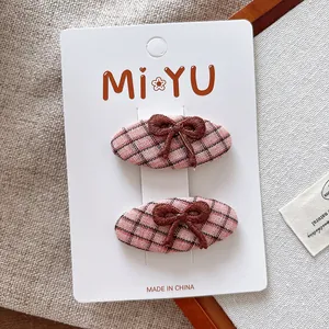 Détail de deux barrettes en tissu à carreaux roses avec nœuds brodés sur fond beige