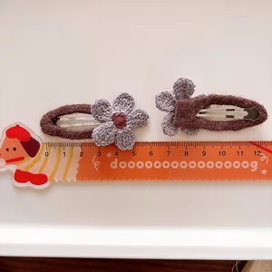 Set of two purple crochet flower hair clips on brown felt base with ruler for size