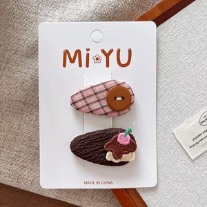 Détail de barrettes à carreaux roses et broderie gâteau à la fraise sur carton