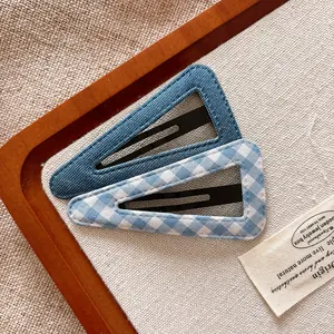 Close-up of blue denim and blue-white checkered fabric triangle hair clips on wood